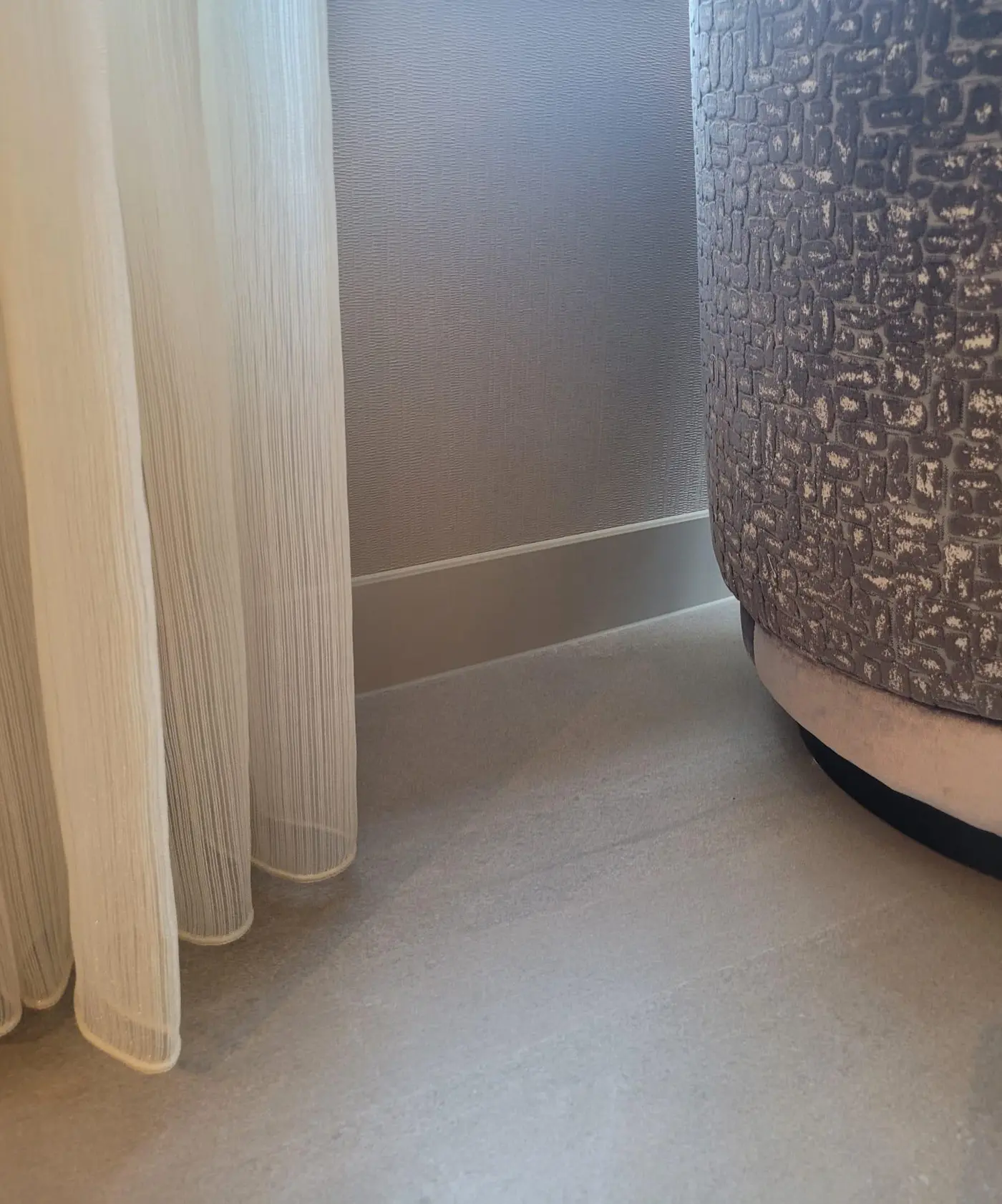 Detail van een hoge taupekleurige plint bij een fauteuil